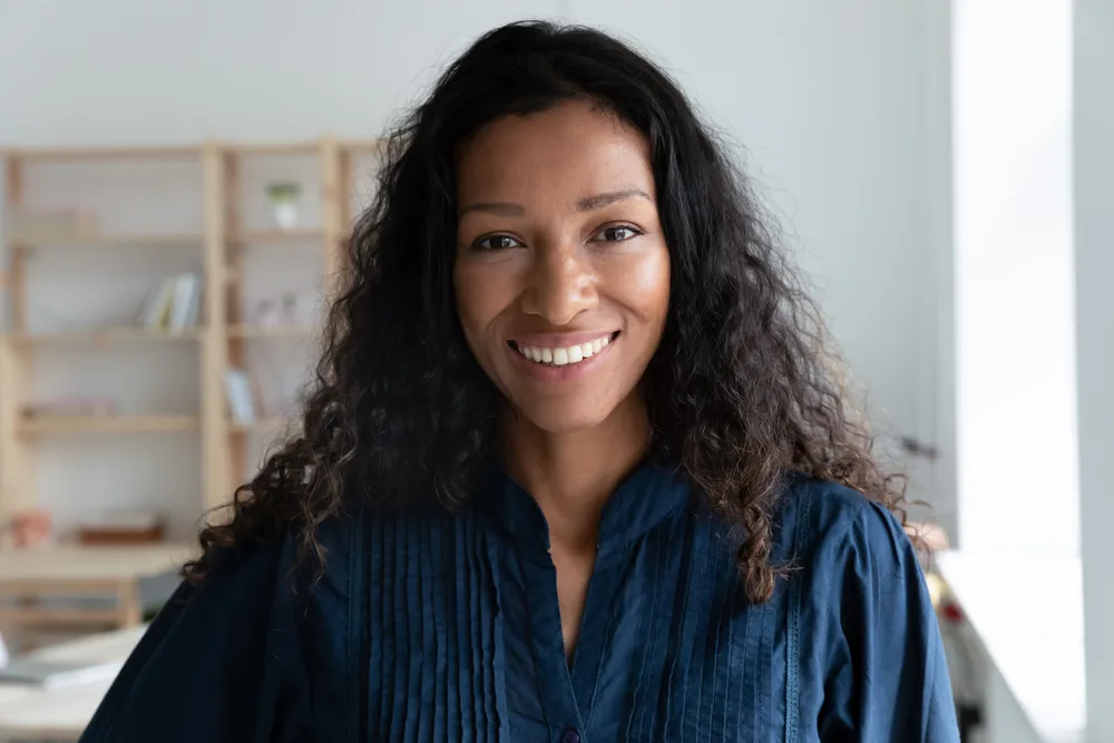 Portrait of a smiling woman with long dark curly hair in a navy blouse