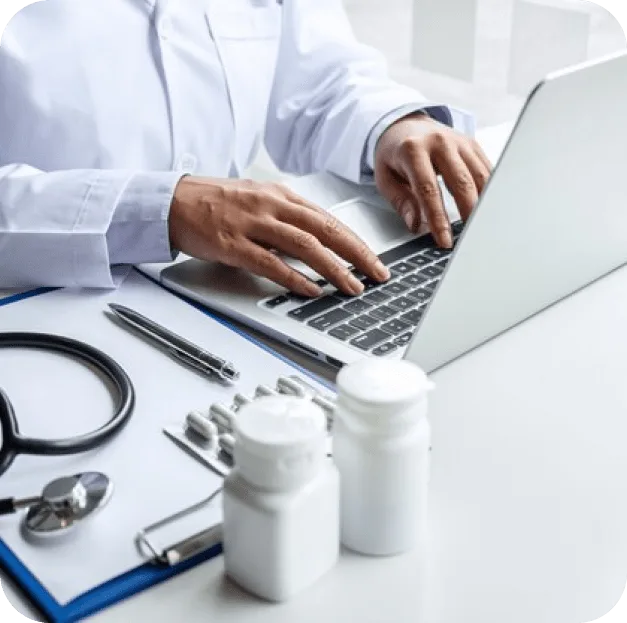 Doctor typing on a laptop next to a stethoscope and pill bottles