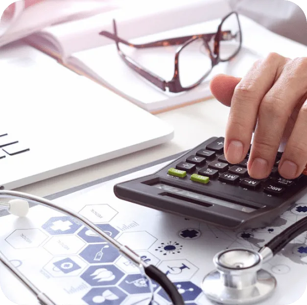 Hand using a calculator beside glasses and medical paperwork