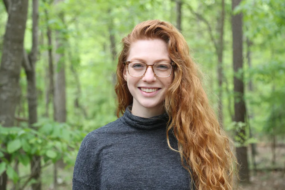 Portrait of a smiling woman with long red hair and glasses in a gray sweater