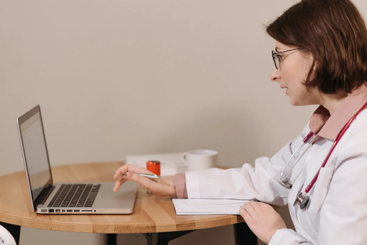 Physician in a white coat updating her credentialing profile on a laptop