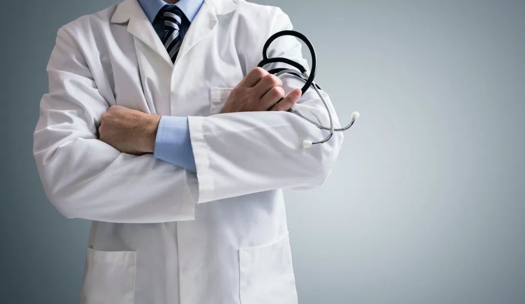 Doctor in a white coat with arms crossed holding a stethoscope